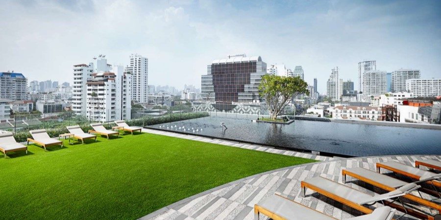 Elegant rooftop pool at Grande Centre Point Sukhumvit 55, adorned with lounge chairs and a backdrop of green grass.